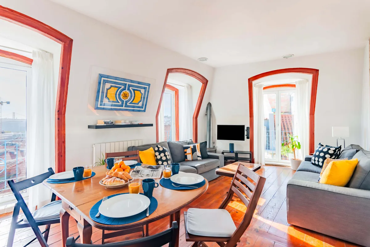 Living room with a breakfast table set in a short-term rental in Lisbon, with a tile panel and doors to the balcony