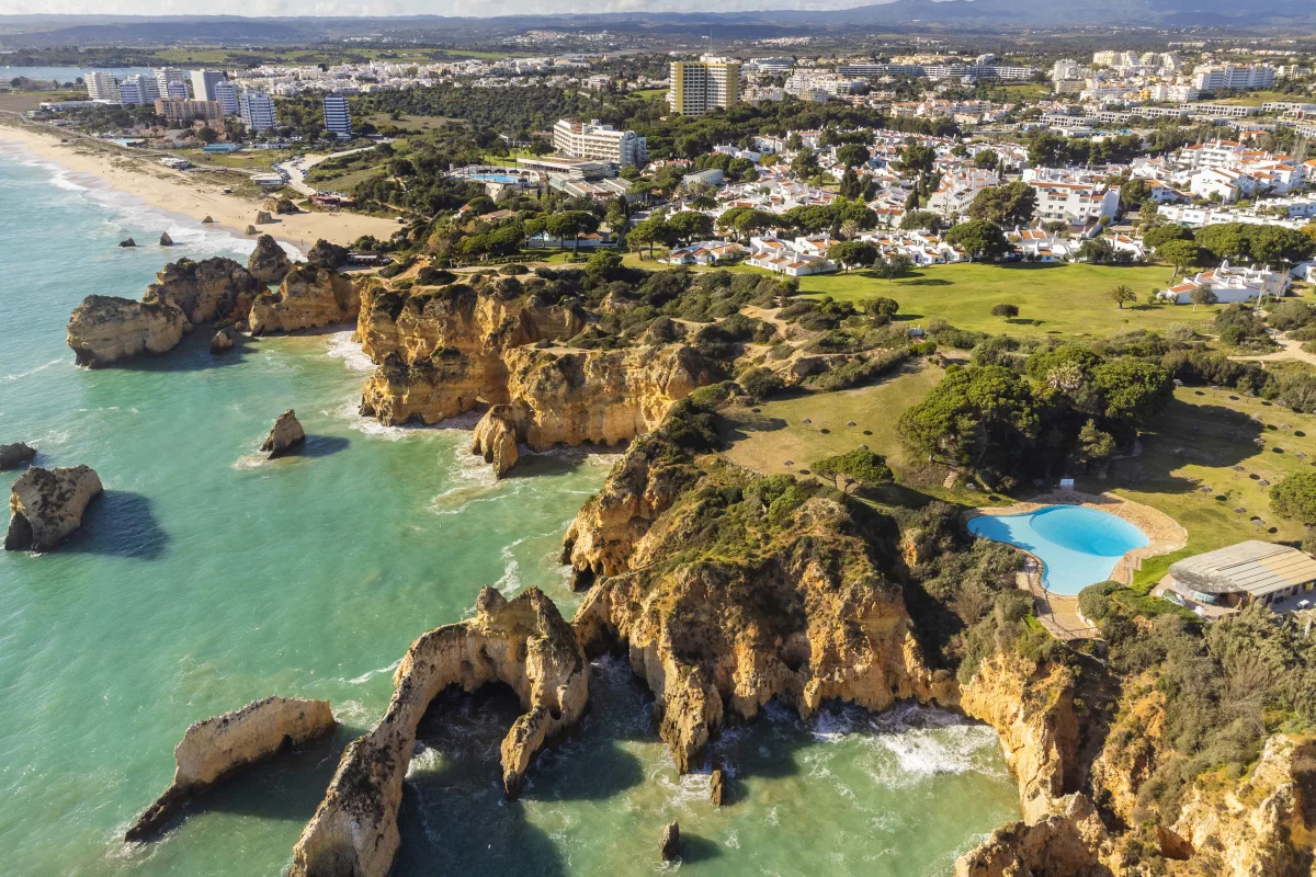 Aerial view of golden cliffs, turquoise sea and a residential development with a pool on the Algarve coast